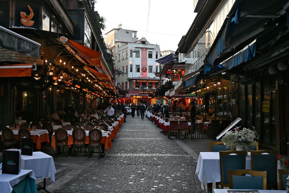 Gasse in Istanbul mit gedeckten Tischen beidseitig und Lichterketten in der Dämmerung