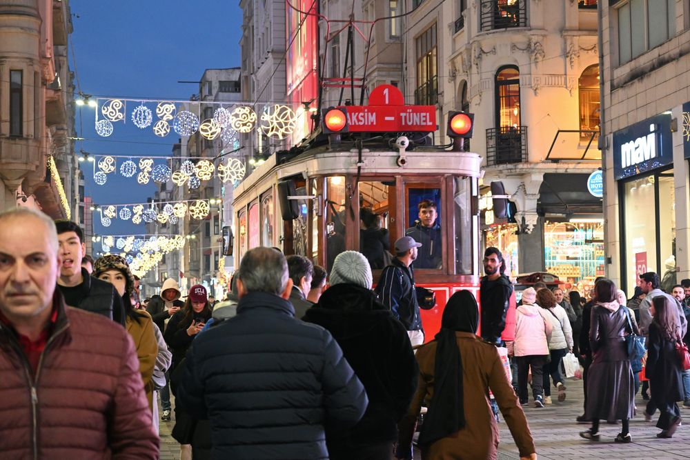 Die İstiklal Caddesi bei Nacht mit der roten Straßenbahn, dichter Menschenmenge und Lichterschmuck