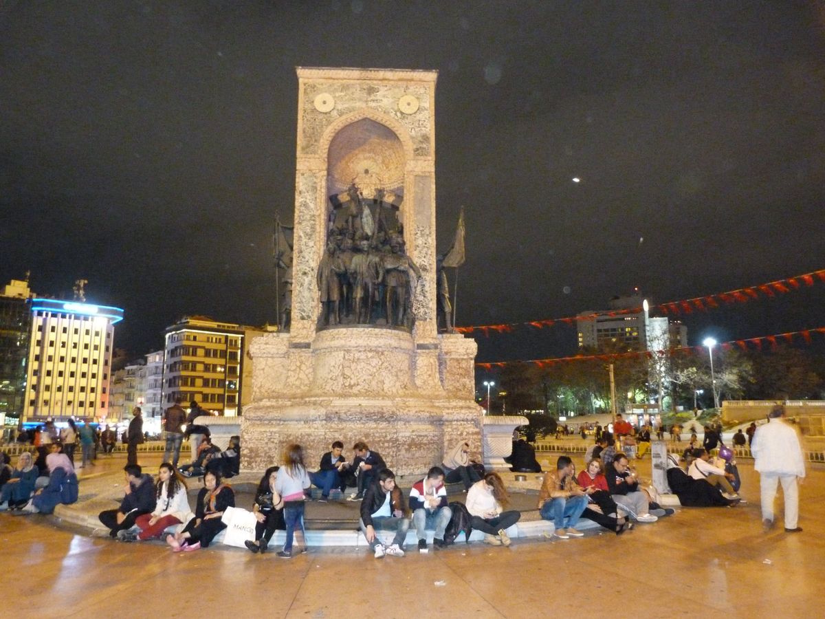 Menschen am Denkmal der Republik auf dem Taksim-Platz bei Nacht