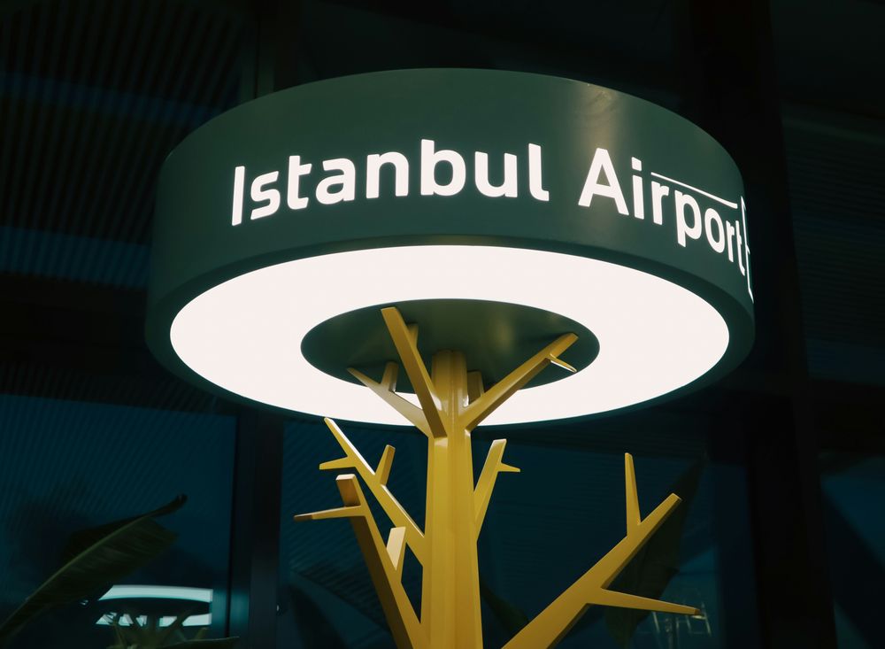 Leuchtschild Istanbul Airport im Terminal, darunter eine gelbe Baumskulptur