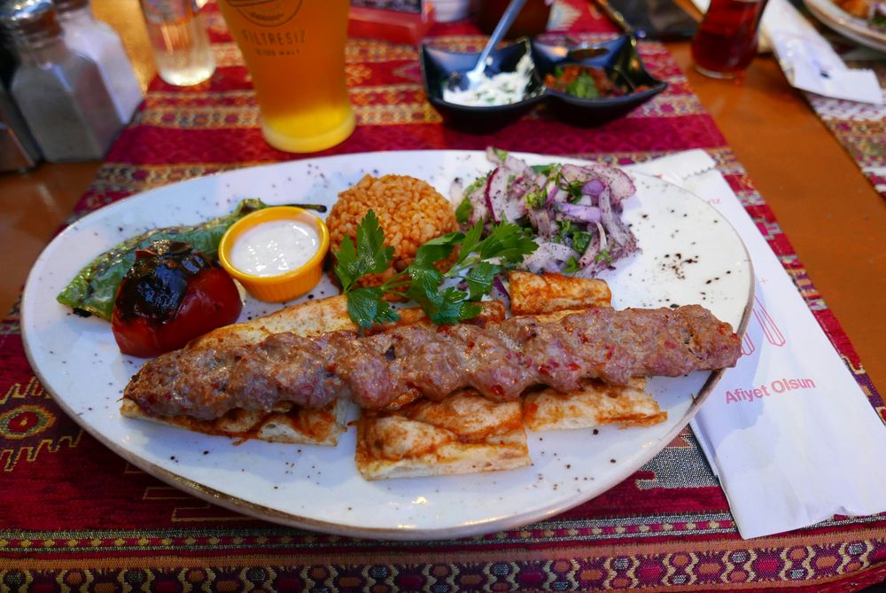 Teller mit Adana Kebab, Bulgur, Salat und Tee in einem Istanbuler Lokal
